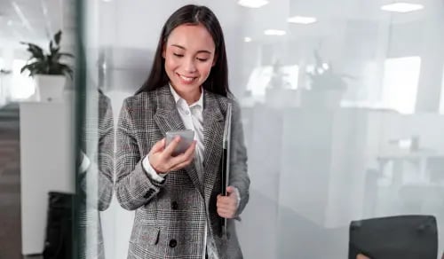 A smiling lawyer consults her mobile phone as she arrives at her glassed-in office. Bigle Legal article on legal tech.