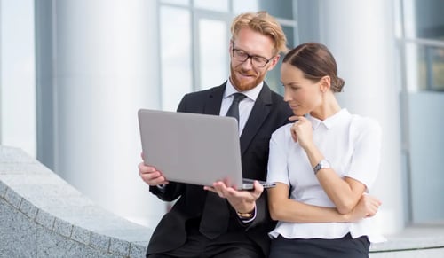 A smiling lawyer in a suit shows his computer to a pensive professional in the procurement department. Bigle Legal CLM article on compliance.