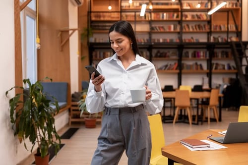 Young lawyer consults her mobile phone while holding a cup of coffee. Bigle Legal blog post to avoid stress thanks to CLM technology.