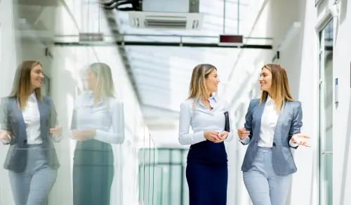 Women lawyers chat in the office corridor next to their reflection. Bigle Legal article on CLM or Contract Lifecycle Management.