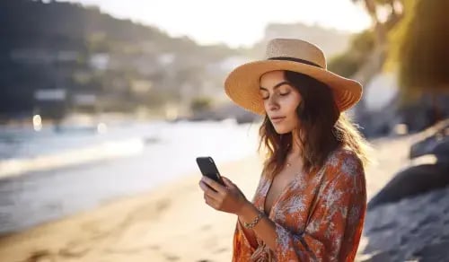 Young woman in summer attire consults her phone on the beach. Bigle Legal article on digital disconnection for in-house lawyers.