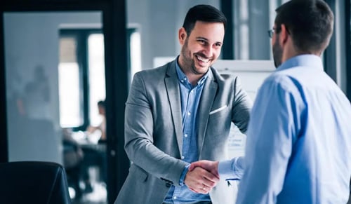 Two men in suits shake hands in an office