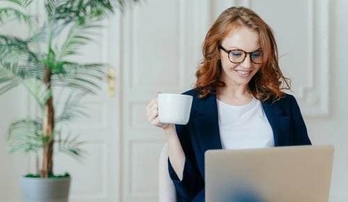 Smiling woman works at her computer with a cup of coffee. Bigle Legal article on legal operations.