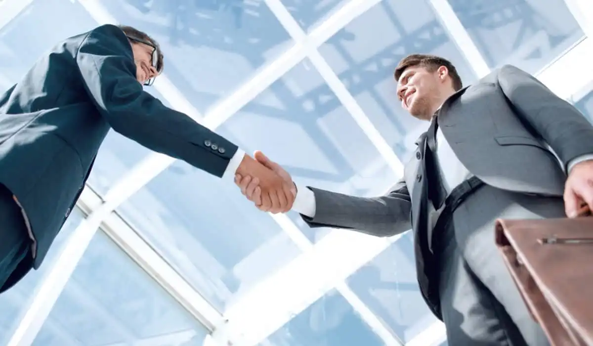 Two men in suits shake hands, smiling. Article on CLM by Bigle Legal.