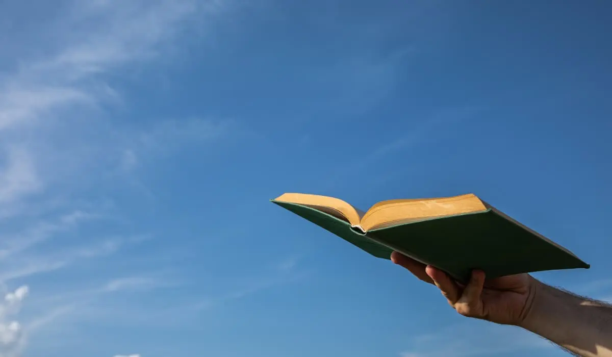 Hand holds an open book under the sky. Bigle Legal article on reading.