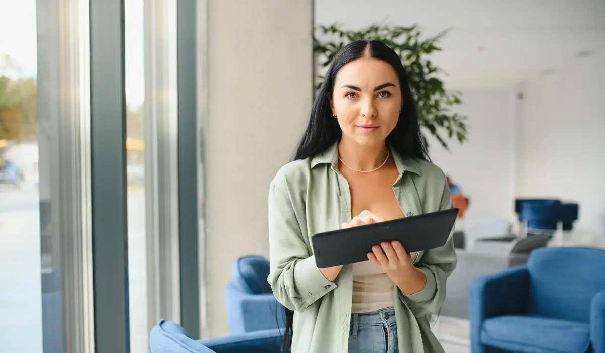 Young woman holds a tablet and smiles in his office. Bigle Legal article on legal team management.