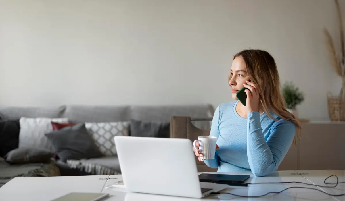 Trabajadora en remoto habla por teléfono mientras sujeta una taza de café. Artículo sobre el teletrabajo de Bigle Legal.