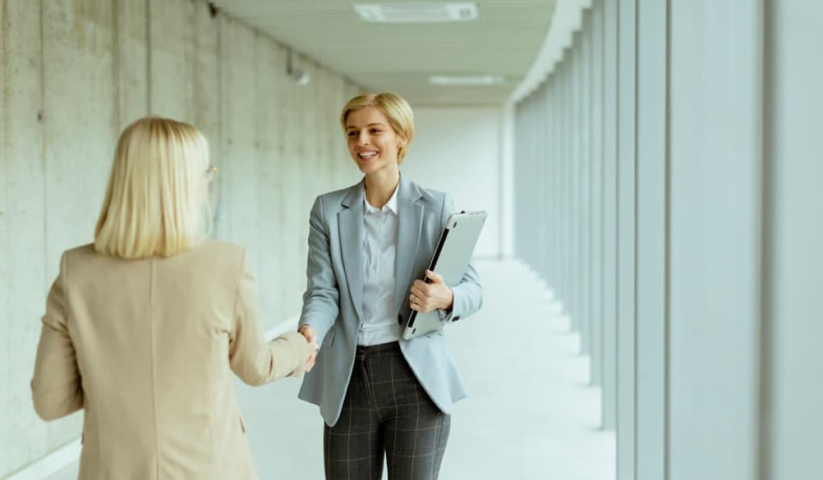 Two smiling lawyers in suits shake hands in a bright corridor. Article by Bigle Legal for the in-house lawyer.